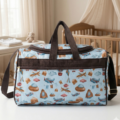 Bolsa maternidade azul-claro com estampas e alças marrons, fotografada de frente sobre mesa branca.