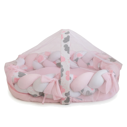 Ninho de bebê rosa e branco com trança e mosquiteiro, em ângulo frontal.